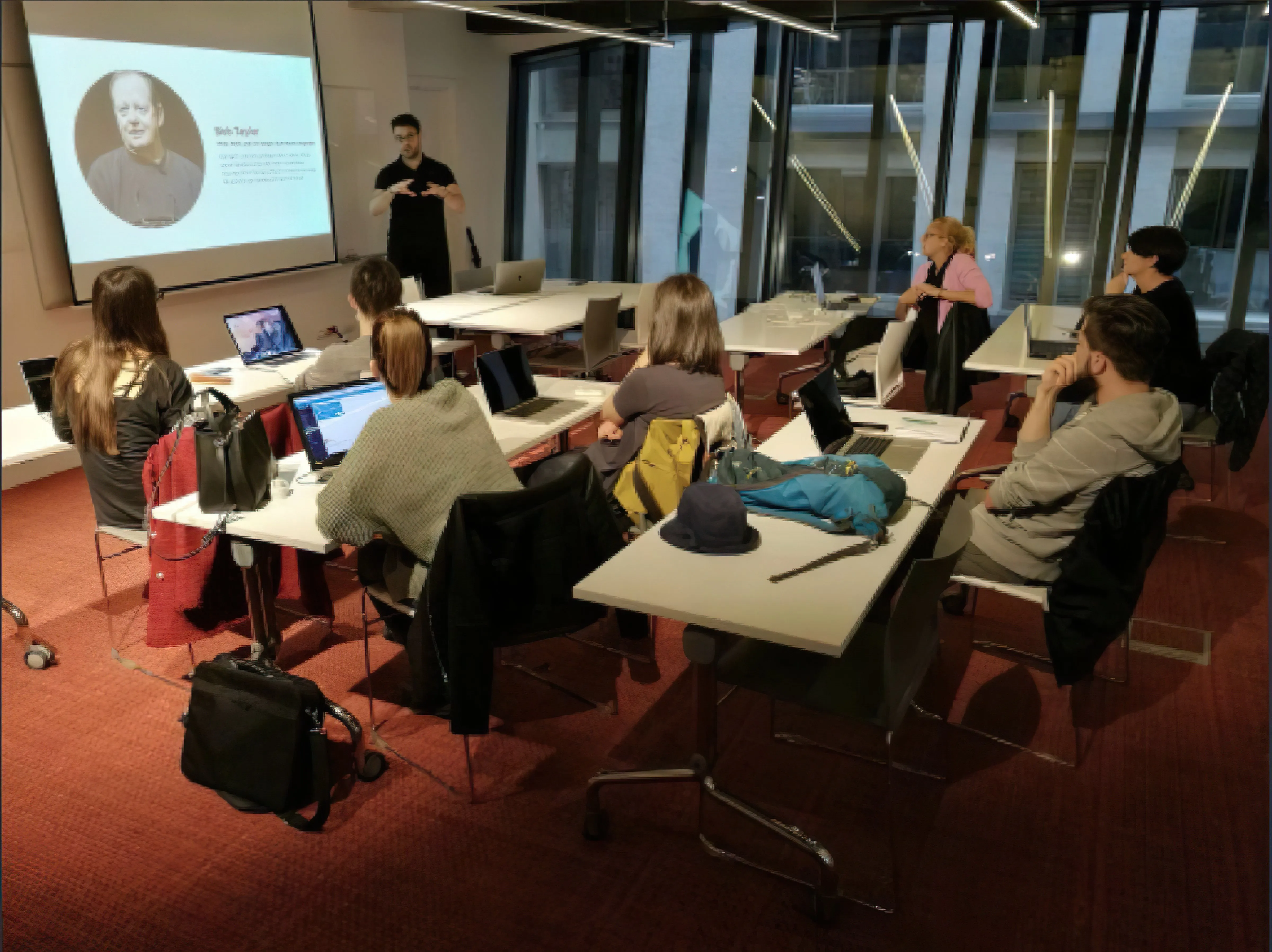 Ash presenting at the front of a classroom to students working on laptops.